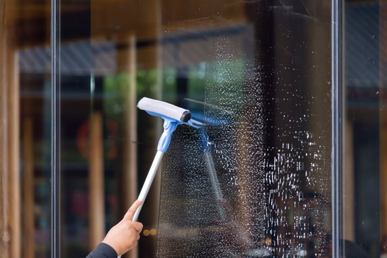 Person cleaning window with squeegee soap and water